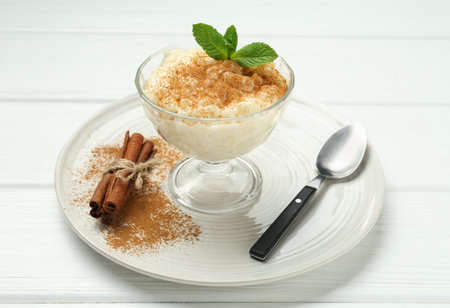 Delicious rice pudding with cinnamon, mint and spoon on white wooden table, closeupの写真素材