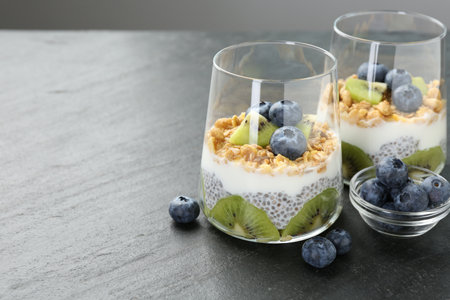 Superfood. Delicious dessert with chia seeds, yogurt, granola, blueberries and kiwi in glasses on gray table, closeup. Space for textの写真素材