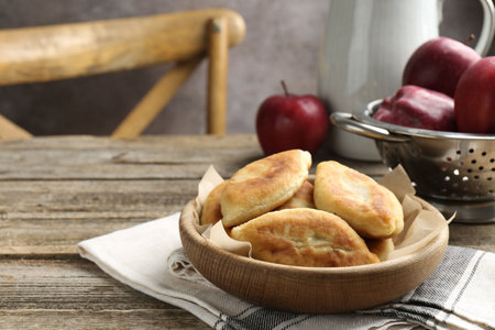 Delicious fried pyrizhky (stuffed pies) and apples on wooden table, closeup. Space for textの写真素材