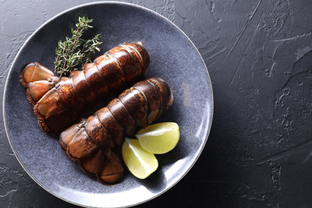 Raw lobster tails, lime and thyme on black table, top view. Space for textの写真素材