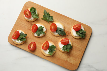 Tasty crackers with cream cheese, tomatoes and parsley on white table, top viewの写真素材