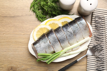 Pieces of herring with lemon slices, green onions and dill on wooden table, flat layの写真素材