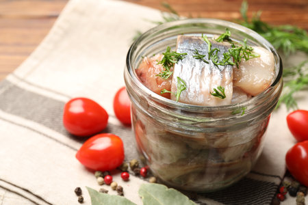 Pieces of delicious herring with dill in jar and tomatoes on table, closeupの写真素材