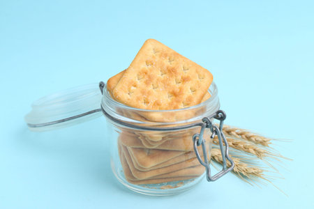Tasty salty crackers and wheat on light blue background, closeup