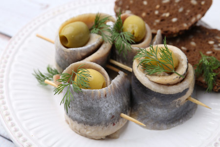 Delicious herring rolls with olives, dill and bread on table, closeup