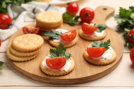 Tasty crackers with cream cheese, tomatoes and parsley on white wooden table, closeupの写真素材