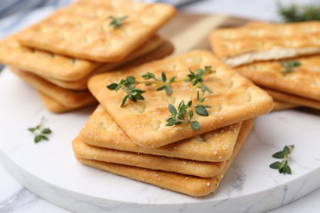 Tasty salty crackers with thyme on white table, closeup