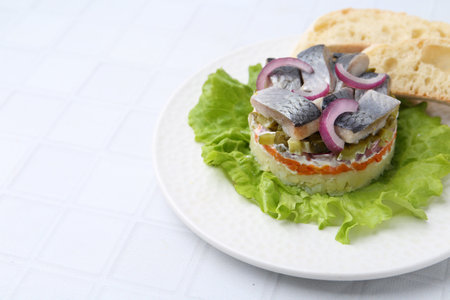 Delicious salad with herring, vegetables and bread on white tiled table, closeup. Space for textの写真素材