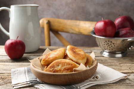 Delicious fried pyrizhky (stuffed pies) and apples on wooden table, closeupの写真素材