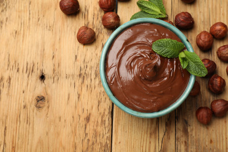 Tasty chocolate hazelnut spread with mint and nuts on wooden table, flat lay. Space for textの写真素材