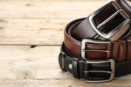 Three leather belts on wooden table, closeup. Space for text