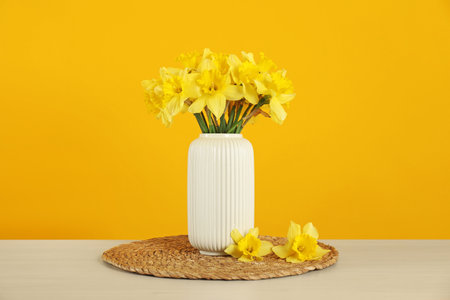 Beautiful daffodils in vase on table against yellow backgroundの写真素材