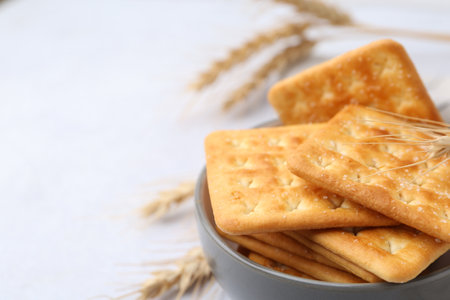 Tasty salty crackers with wheat on white table, closeup. Space for textの写真素材