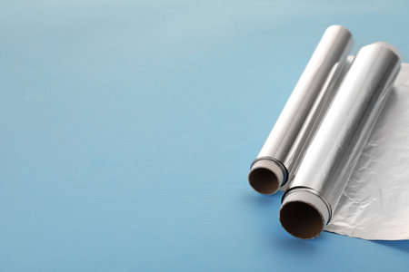 Rolls of aluminum foil on light blue background, closeup. Space for textの写真素材