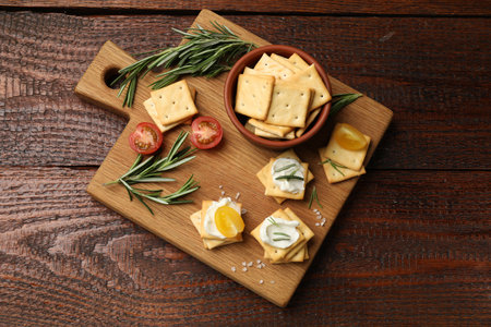 Tasty crackers with cream cheese, rosemary, salt and tomatoes on wooden table, top viewの写真素材