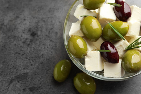 Tasty olives with feta cheese in glass bowl on grey textured table, closeup. Space for textの写真素材