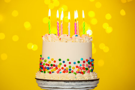 Tasty cake with colorful sprinkles and candles on yellow background, bokeh effectの写真素材