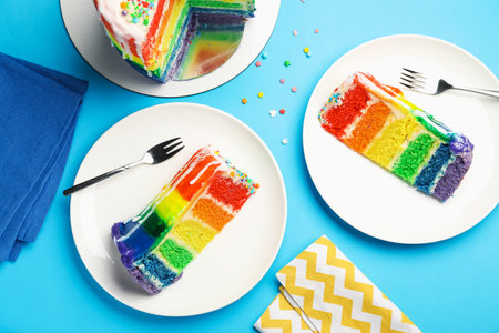 Pieces of delicious rainbow cake and sprinkles served on light blue table, flat layの写真素材