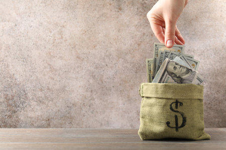 Woman taking dollar banknote from bag at wooden table, closeup. Space for textの写真素材