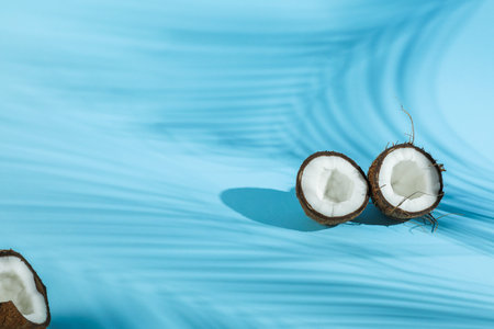 Fresh coconuts and shadow cast by tropical palm on light blue background. Space for text
