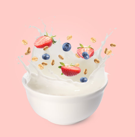 Oat flakes with fresh berries and milk splashing out from bowl on pink backgroundの写真素材