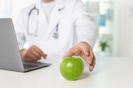 Nutritionist taking green apple at table in clinic, closeupの写真素材
