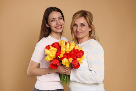 Woman giving her mother flowers on beige backgroundの写真素材