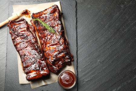 Tasty roasted pork ribs served with rosemary and sauce on black table, top view. Space for textの写真素材