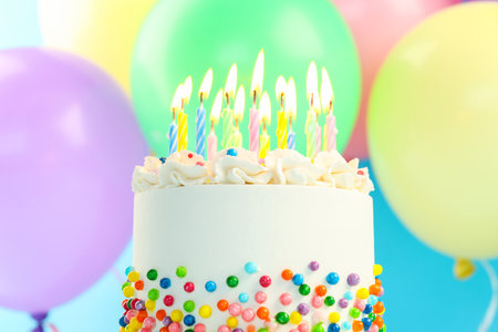 Delicious bento cake with sprinkles, candles and colorful balloons on light blue background, closeupの写真素材