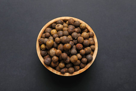 Aromatic allspice in bowl on dark table, top view