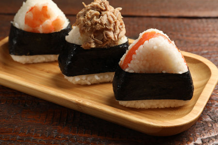 Tasty onigiri (Japanese rice balls) served on wooden table, closeup