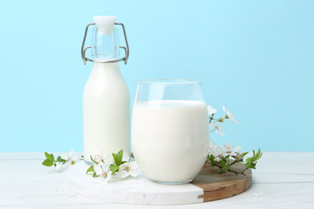 Fresh milk and blossoms on white table against light blue backgroundの写真素材