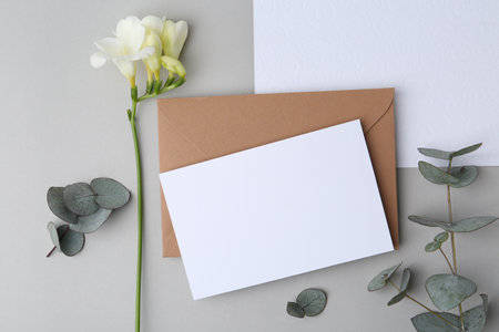 Blank greeting card, paper envelope, flower and eucalyptus leaves on light grey background, flat layの写真素材