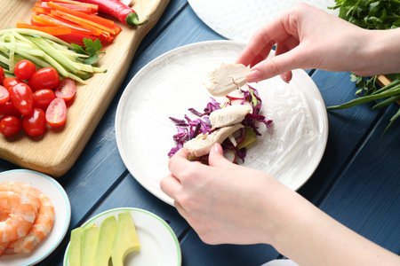 Woman making tasty spring roll at blue wooden table, above view