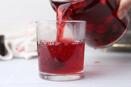 Pouring tasty cherry compot into glass on white tiled table, closeupの写真素材