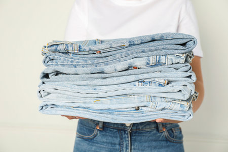 Woman with stack of different stylish jeans near light wall indoors, closeupの写真素材