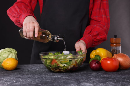 Woman pouring oil onto tasty salad at dark textured table, closeupの写真素材