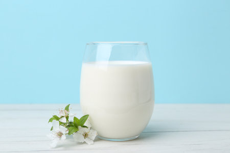Glass of fresh milk and blossoms on white wooden table against light blue backgroundの写真素材