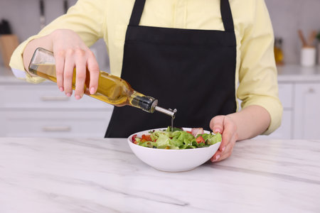 Woman pouring oil onto tasty salad at white marble table in kitchen, closeupの写真素材