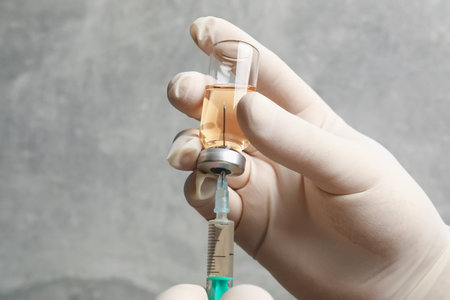 Doctor filling syringe with hepatitis vaccine from glass vial against grey background, closeup. Space for textの写真素材