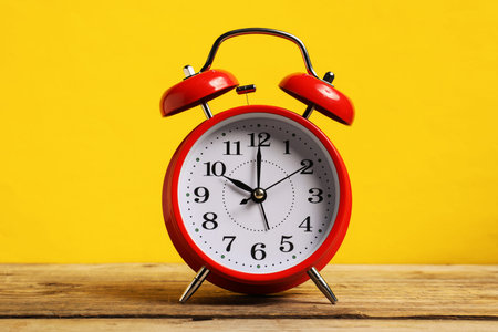 One red alarm clock on wooden table against yellow background