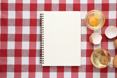 Blank recipe book, egg and oil on checkered tablecloth, flat lay. Space for textの写真素材