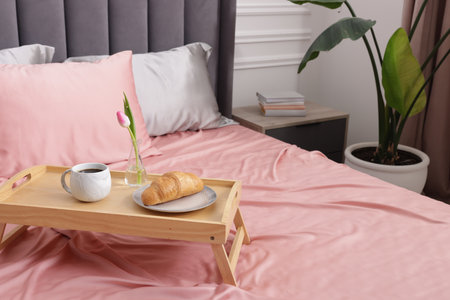 Aromatic coffee, croissant and tulip on bed with beautiful silk linens indoorsの写真素材