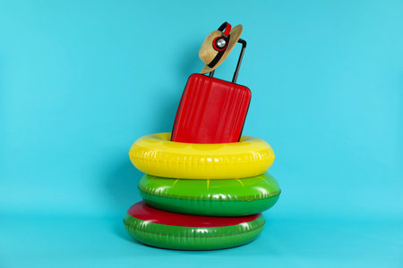 Colorful inflatable rings, suitcase, straw hat and headphones on light blue background