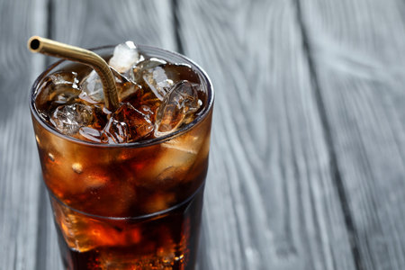Refreshing cola with ice cubes and straw in glass on blurred grey background, closeup. Space for...
