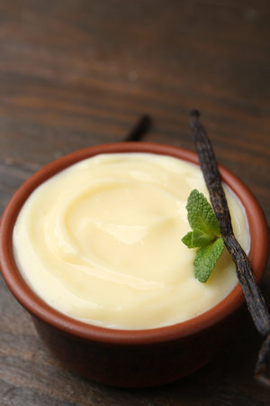 Tasty vanilla pudding, mint and pods on wooden table, closeup
