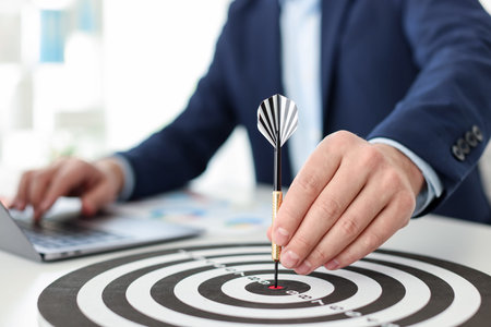 Man with dart aiming at dartboard while working indoors, closeup