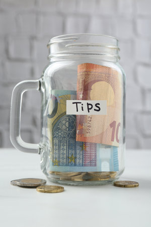 Tips jar with money on white tableの写真素材