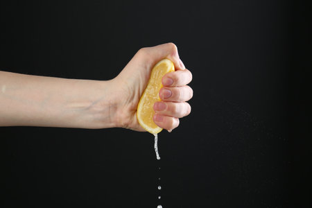 Woman squeezing lemon on black background, closeup. Space for textの写真素材