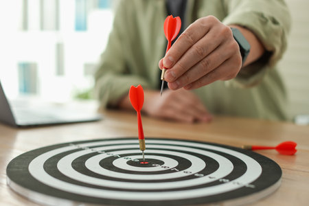 Man with dart aiming at dartboard while working indoors, closeup